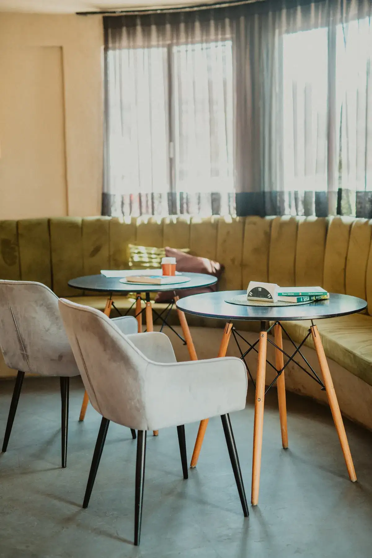 Lounge com banco estofado verde, mesas redondas e poltronas